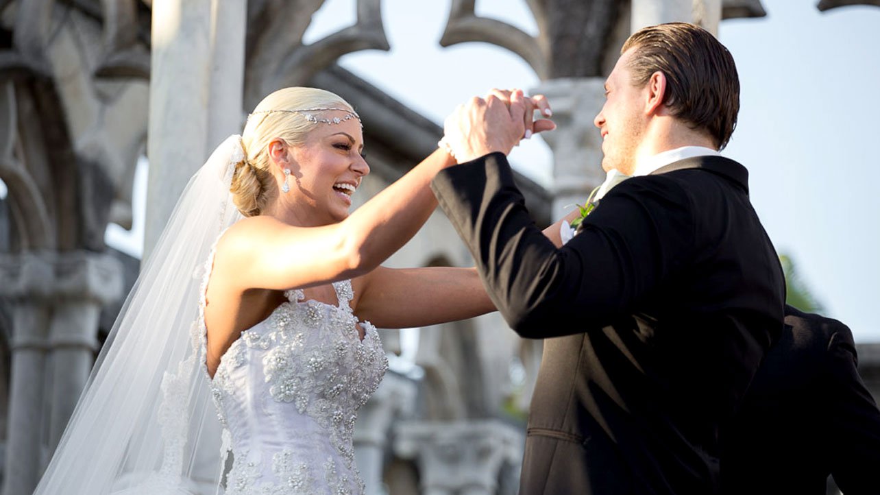 La sposa in una corona con un bouquet si erge su un tappeto bianco vicino a  un arco nuziale