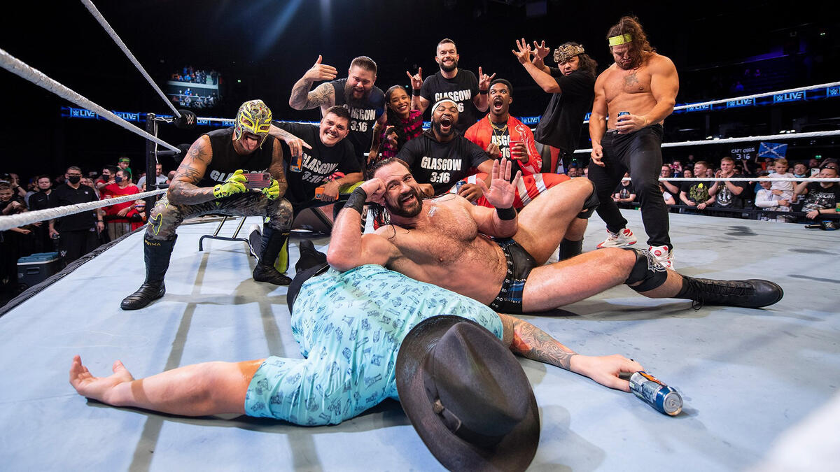  An image of a group of wrestlers in the ring celebrating with the Glasgow crowd wearing controversial shirts that say 'Glasgow 3:16'.